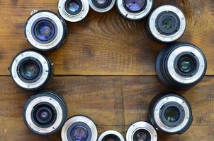 Several photographic lenses lie on a brown wooden background. Space for text photo