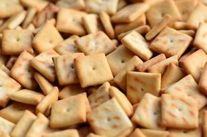 A lot of small cookies are square shaped. A pattern of a yellow salt cracker. Background image with salted pastry photo