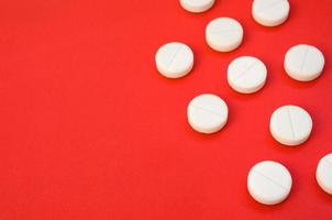 A few white tablets lie on a bright red background surface. Background image on medical and pharmaceutical topics photo