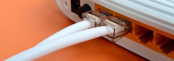los enchufes del cable de Internet están conectados al enrutador de Internet, que se encuentra sobre un fondo naranja brillante. elementos necesarios para la conexión a internet foto