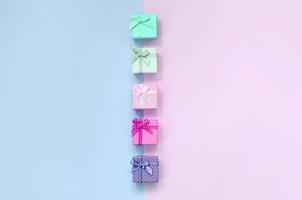 pequeñas cajas de regalo de diferentes colores con cintas se encuentran sobre un fondo violeta y rosa foto