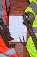 una hoja de papel arrugada con dos lápices rodeada de uniformes de trabajo verdes y naranjas y llaves ajustables foto