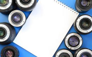 Several photographic lenses and white notebook lie on a bright blue background. Space for text photo