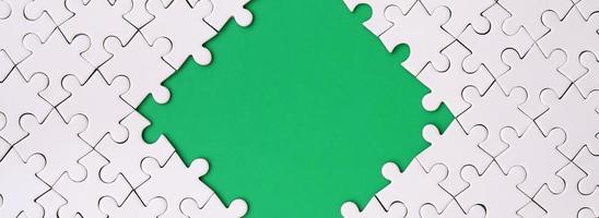 Framing in the form of a rhombus, made of a white jigsaw puzzle around the green space photo