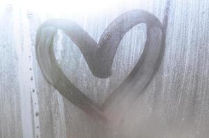 un dibujo en forma de corazón dibujado por un dedo en un vidrio empañado en tiempo lluvioso foto