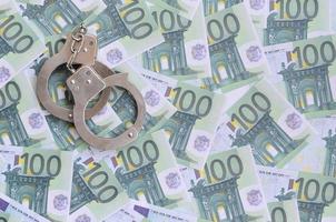 Police handcuffs lies on a set of green monetary denominations of 100 euros. A lot of money forms an infinite heap photo