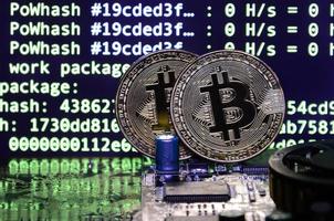 Two bitcoins lies on a videocard surface with background of screen display of cryptocurrency mining by using the GPUs photo