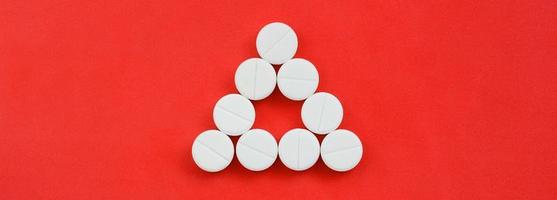 Several white tablets lie on a bright red background in the form of an even triangle. Background image on medicine and pharmaceutical topics photo