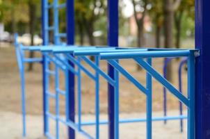 Blue metal pipes and cross-bars against a street sports field for training in athletics. Outdoor athletic gym equipment. Macro photo with selective focus and extremely blurred background