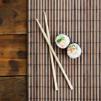 Sushi rolls and wooden chopsticks lie on a bamboo straw serwing mat. Traditional Asian food. Top view. Flat lay minimalism shot with copy space photo