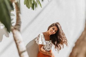 Curly woman in great mood, posing on white background with trees. Lady in white floral print top sm