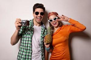 pareja activa en trajes de verano brillantes y gafas de sol posando con cámara retro y piña. chica foto