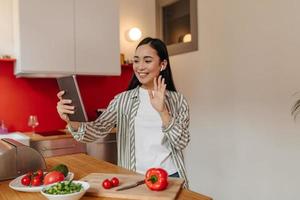 Girl was distracted from cooking vegetable salad and talking via video link in tablet