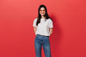 Girl in orange sunglasses is smiling on red background