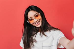 Woman in great mood and in orange glasses takes selfie on red background photo