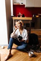 Smiling photographer sitting on floor. Indoor shot of woman with camera expressing positive emotion photo