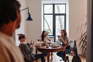 enfoque selectivo del hombre mirando a las chicas bebiendo té. amigos con café y laptop sentados a la mesa en casa foto
