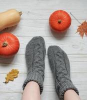 Legs of a girl in knitted socks on a wooden background next to pumpkins and autumn leaves photo