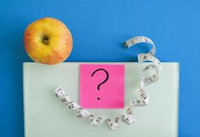 Electronic scales, a sticker with a question mark, an apple and a centimeter tape photo