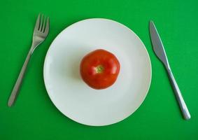 tomate en un plato, tenedor y cuchillo foto