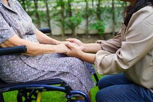 cuidador ayuda a una anciana asiática con discapacidad a una paciente sentada en silla de ruedas en el parque, concepto médico. foto