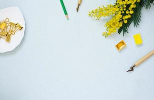 borde, pancarta de lápices de colores, acuarelas, ramas de mimosa y una pluma sobre un fondo azul. copia espacio para un blogger, artista o calígrafo foto