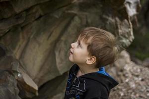 A boy-child on the background of a rocky mountain looks at something with curiosity and is surprised. Nature, rocks, mountains. photo