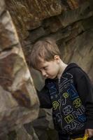 A boy-child on the background of a rocky mountain looks at something with curiosity and is surprised. Nature, rocks, mountains. photo