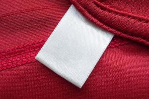 etiqueta de ropa blanca en blanco para el cuidado de la ropa en el fondo de la camisa deportiva de poliéster rojo foto