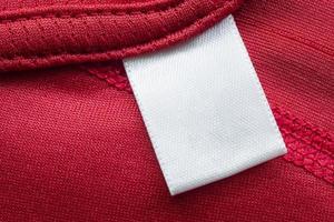 White blank laundry care clothes label on red polyester sport shirt background photo