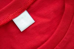 etiqueta de etiqueta de ropa en blanco blanco sobre fondo de textura de tela de camisa de algodón rojo nuevo foto