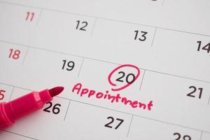 Red color marker pen pointing at important appointment schedule on white calendar page date close up photo