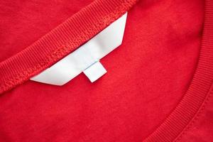 White blank clothing tag label on new red cotton shirt fabric texture background photo