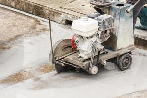 Worker using diamond saw blade machine cutting concrete road at construction site photo