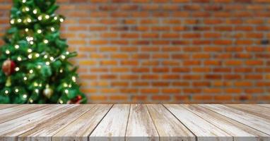 Empty wood table top with blur decorated Christmas tree with baubles on brick wall background photo