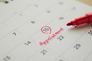 Red color marker pen pointing at important appointment schedule on white calendar page date close up photo