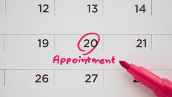 Red color marker pen pointing at important appointment schedule on white calendar page date close up photo