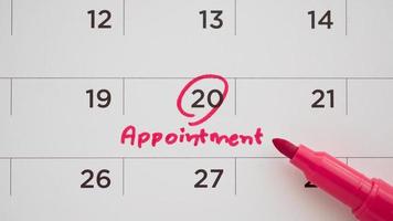 Red color marker pen pointing at important appointment schedule on white calendar page date close up photo