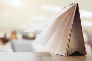 Calendar page flipping sheet on wood table with blurred office interior background business schedule planning appointment meeting concept photo