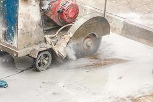 Worker using diamond saw blade machine cutting concrete road at construction site photo