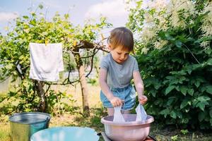 la niña de preescolar ayuda con la lavandería. niño lava ropa en el jardín foto