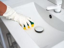 a hand in a white rubber glove with a sponge washes a white sink photo