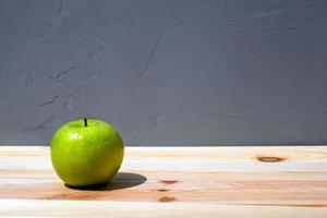 A fresh tasty green apple on a natural wood table with a rough concrete surface on a background with a copy space photo