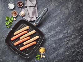 Raw meat sausages on square grill pan, with herbs and spices. Top view photo