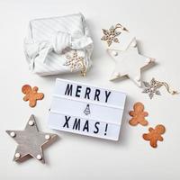 Light box inscription Merry Christmas, gifts in Japanese furoshiki style and gingerbread cookies photo