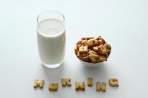 A glass of milk, a bowl of cookies with inscription from the cookies on the white background. photo