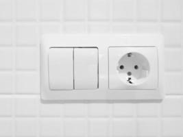 New white switch and socket on a tiled wall photo
