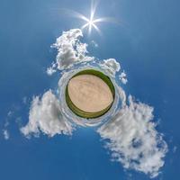 tiny planet in blue sky with beautiful clouds with transformation of spherical panorama 360 degrees. Spherical abstract aerial view. Curvature of space. photo