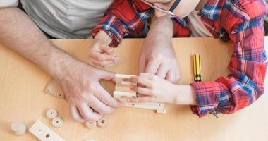 Happy father's day and childhood concept. Close-up of a father and a boy son in glasses work with hand tools, using a screwdriver, assembling a wooden house constructor at the table. photo