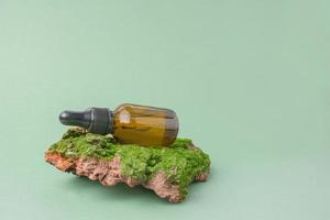 Natural skin care. Environmentally friendly cosmetics. brown glass jar with facial serum on the bark of a tree with green moss on a green background. copy space photo